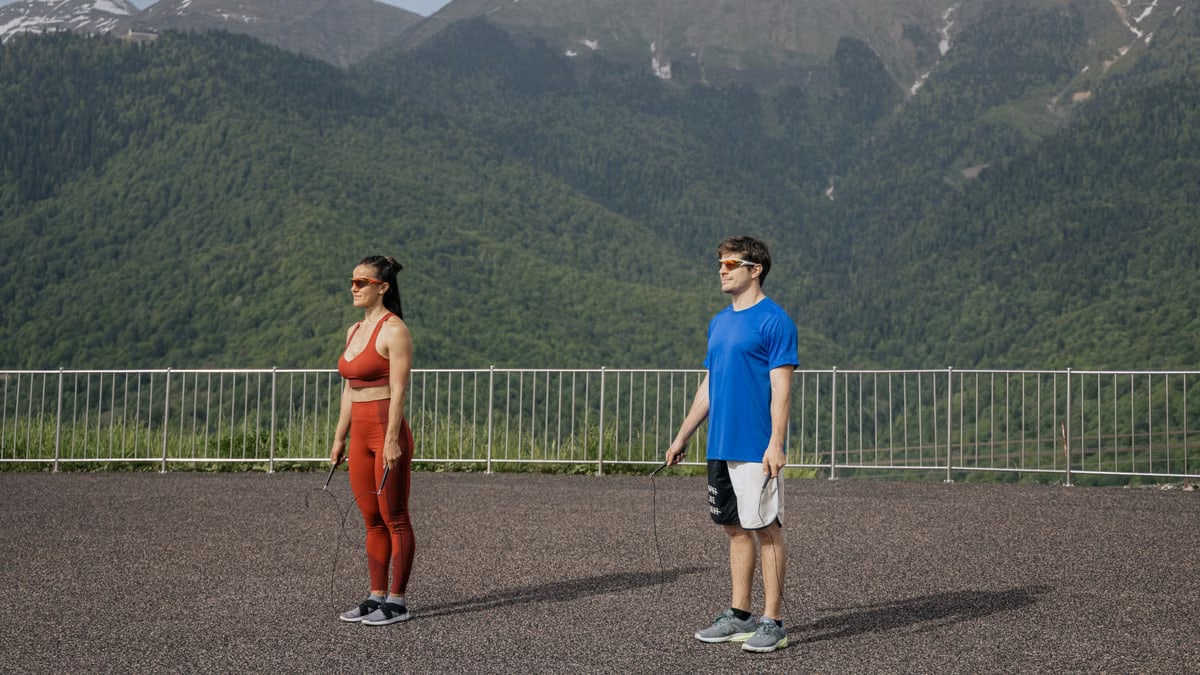 Two athletes exercise with jump ropes in a mountain setting, showcasing outdoor fitness and recreation.
