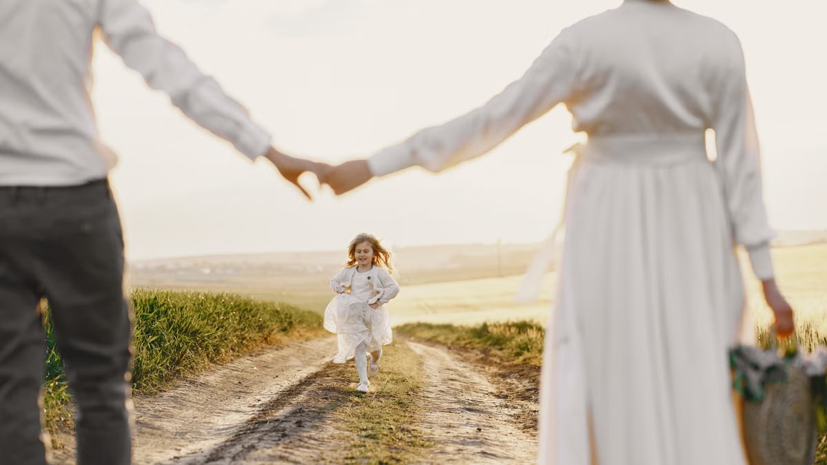 A joyful child runs toward parents holding hands on a sunny rural path.